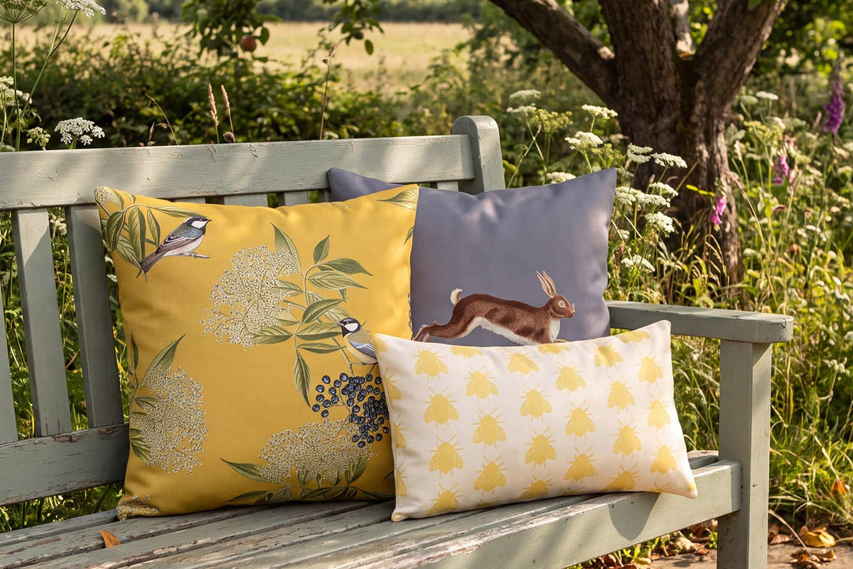 Mustard bird, grey hare and cream bee outdoor cushions on a painted bench in the British countryside