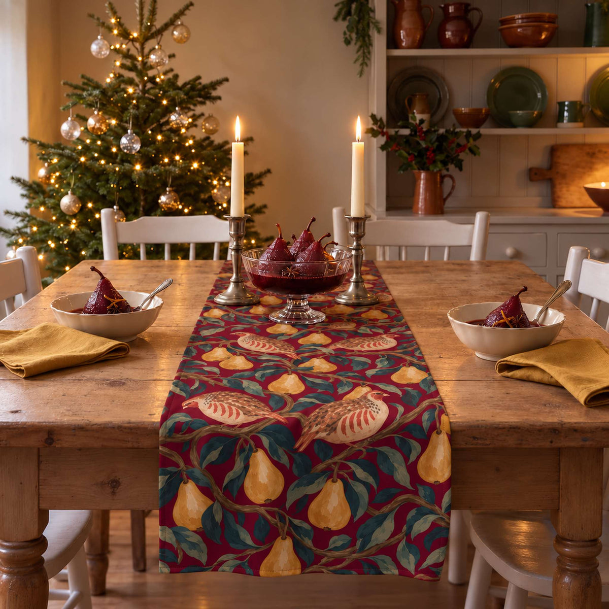 Partridge and Pear Christmas table runner in Burgundy, styled on a wooden table with a softly draped end in a candlelit Christmas room.