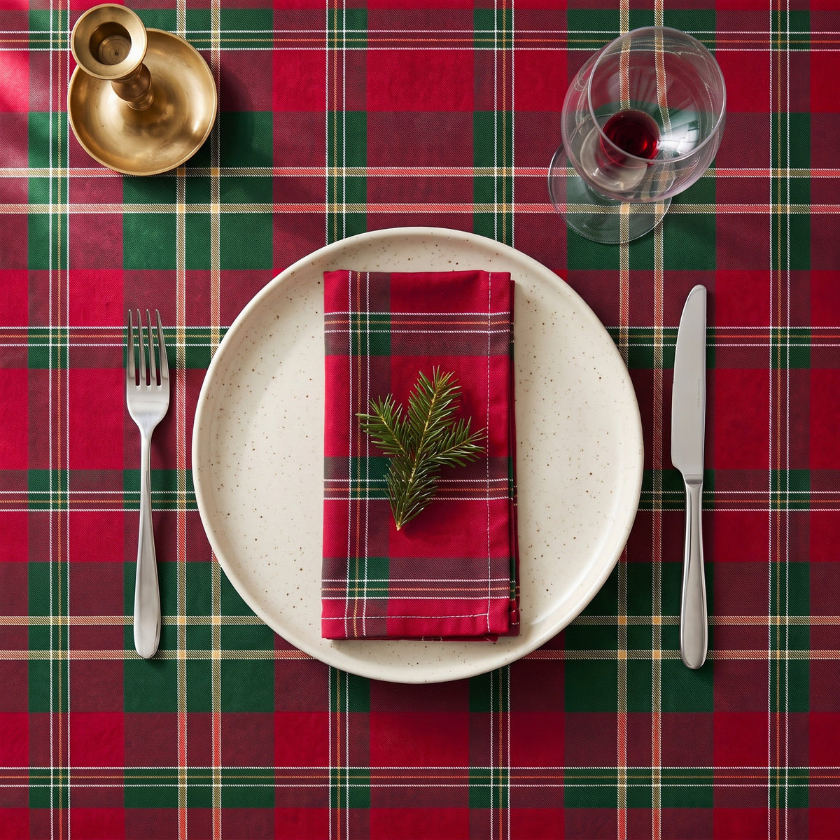 Burgundy tartan Christmas napkin folded on a cream plate with a sprig of pine, on a matching tablecloth