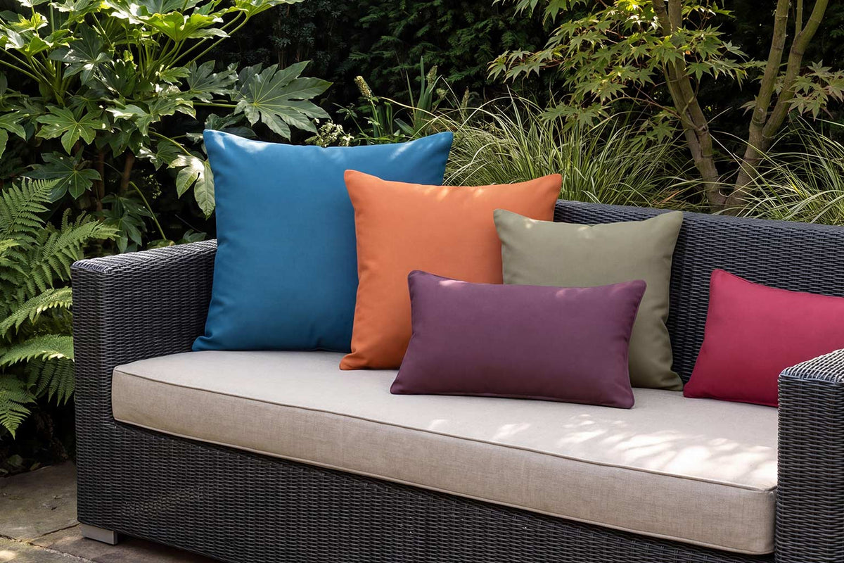 Colourful plain outdoor cushions in blue, orange, olive, grape and raspberry on a dark rattan garden sofa
