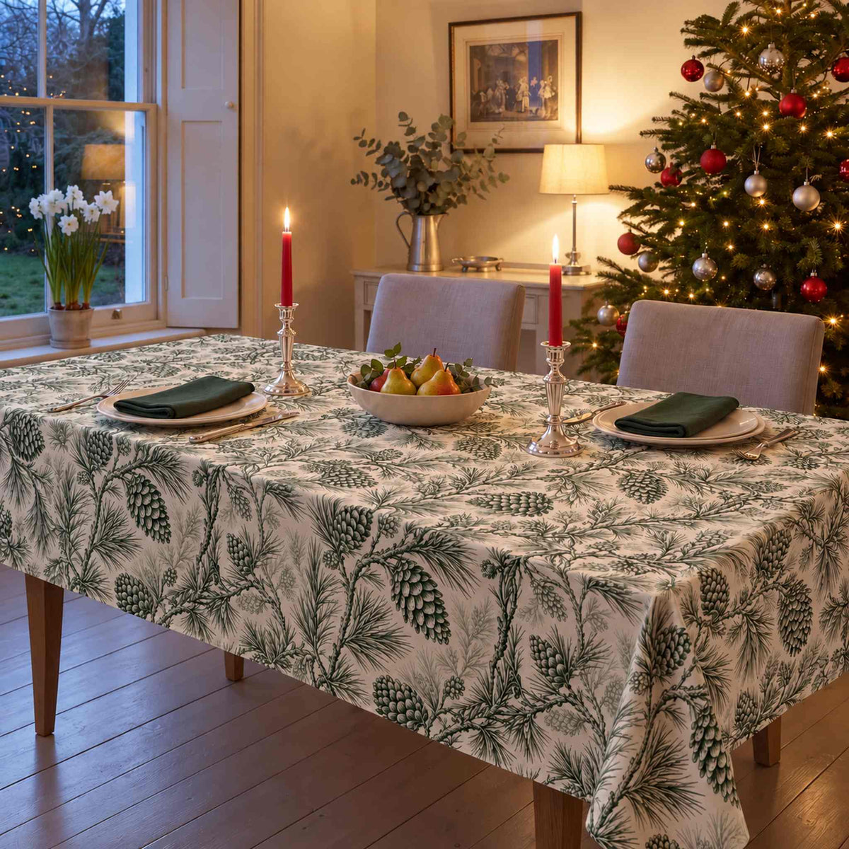 Green on ivory Pine Bough Christmas tablecloth draped over a dining table with green napkins, ivory plates, pears and candles in a pale Georgian room.