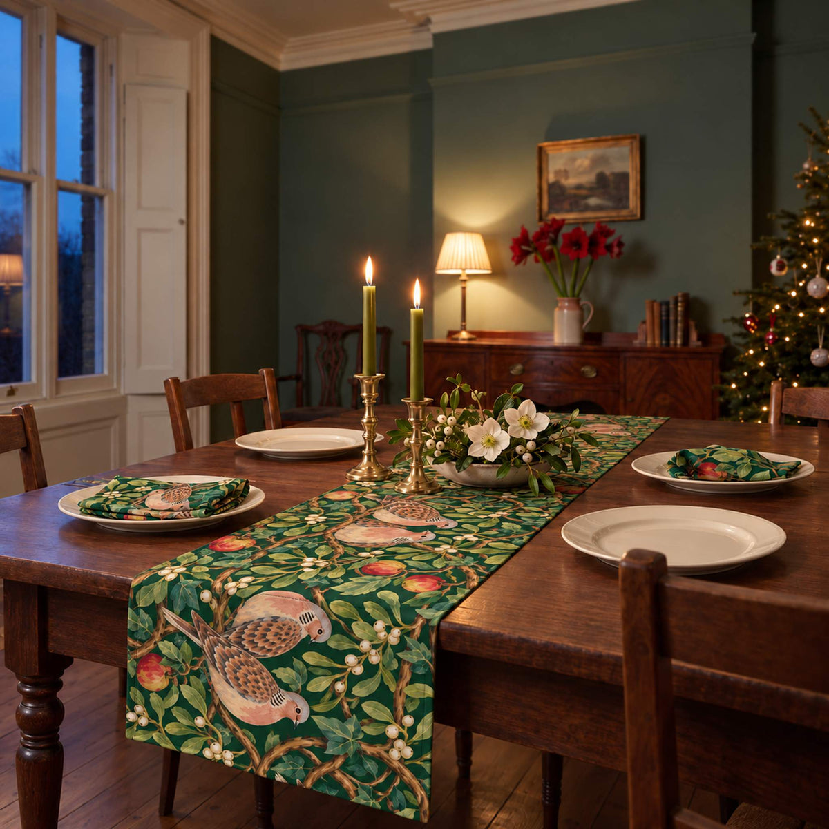 Turtle Doves and Mistletoe Christmas table runner in Green on a bare wooden table in a candlelit Christmas dining room.
