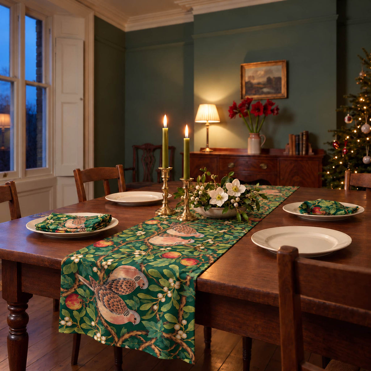 Turtle Doves and Mistletoe Christmas table runner in Green, styled on a wooden table with a softly draped end in a candlelit Christmas room.