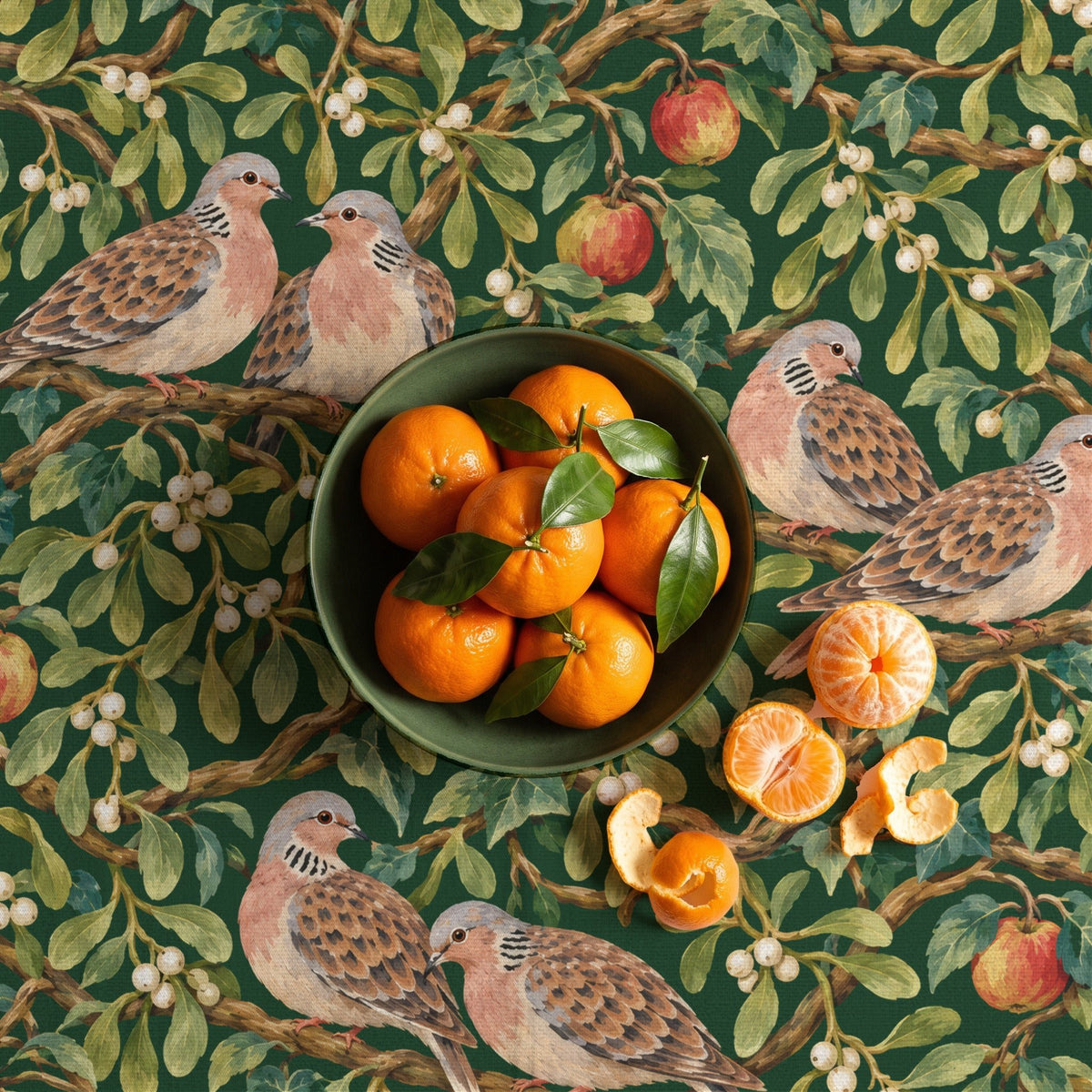 Turtle Doves and Mistletoe Christmas tablecloth in green seen from above, with a green bowl of clementines with their leaves and two peeled clementines and their peel beside it