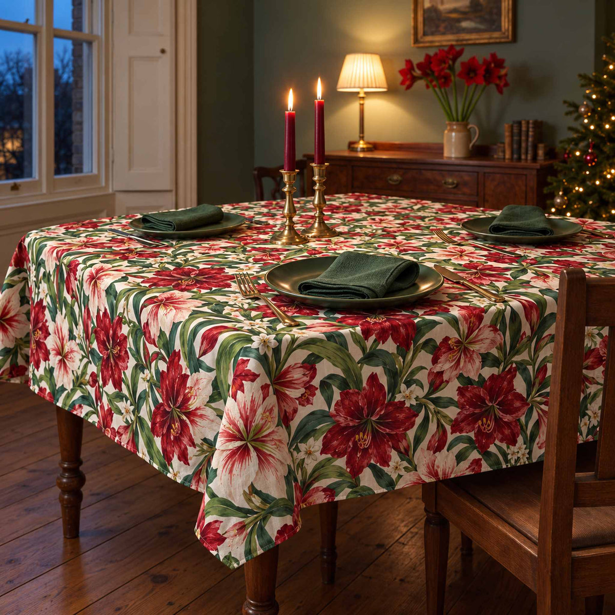 Ivory Amaryllis Christmas tablecloth draped over a dining table with green place settings and red candles in a green Victorian dining room.