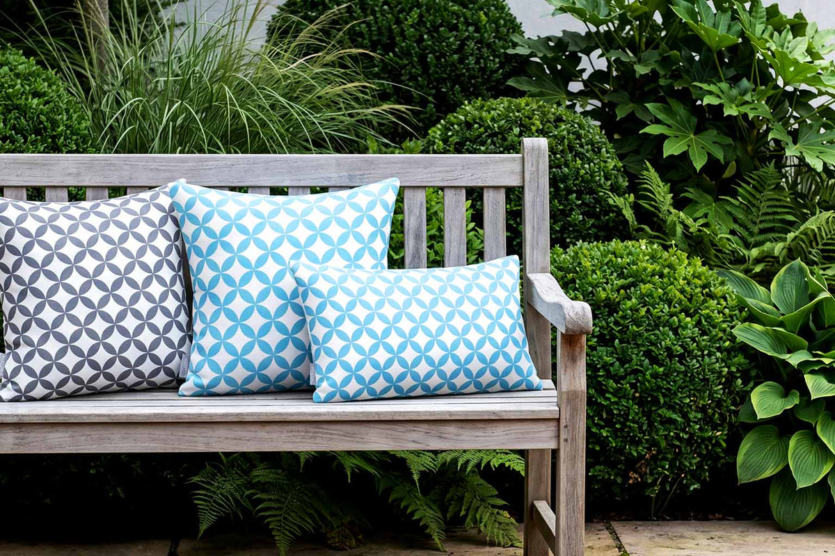 Blue and grey Bahia Marrakech outdoor cushions on a weathered teak bench in a British courtyard garden