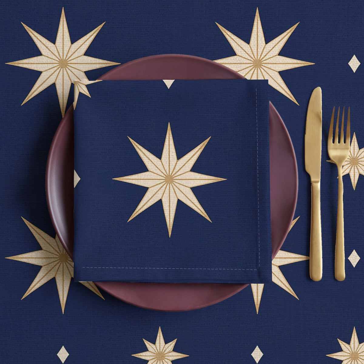 Navy and gold Stars Christmas napkin folded in four on a plum plate, laid on the matching Stars tablecloth with brass cutlery