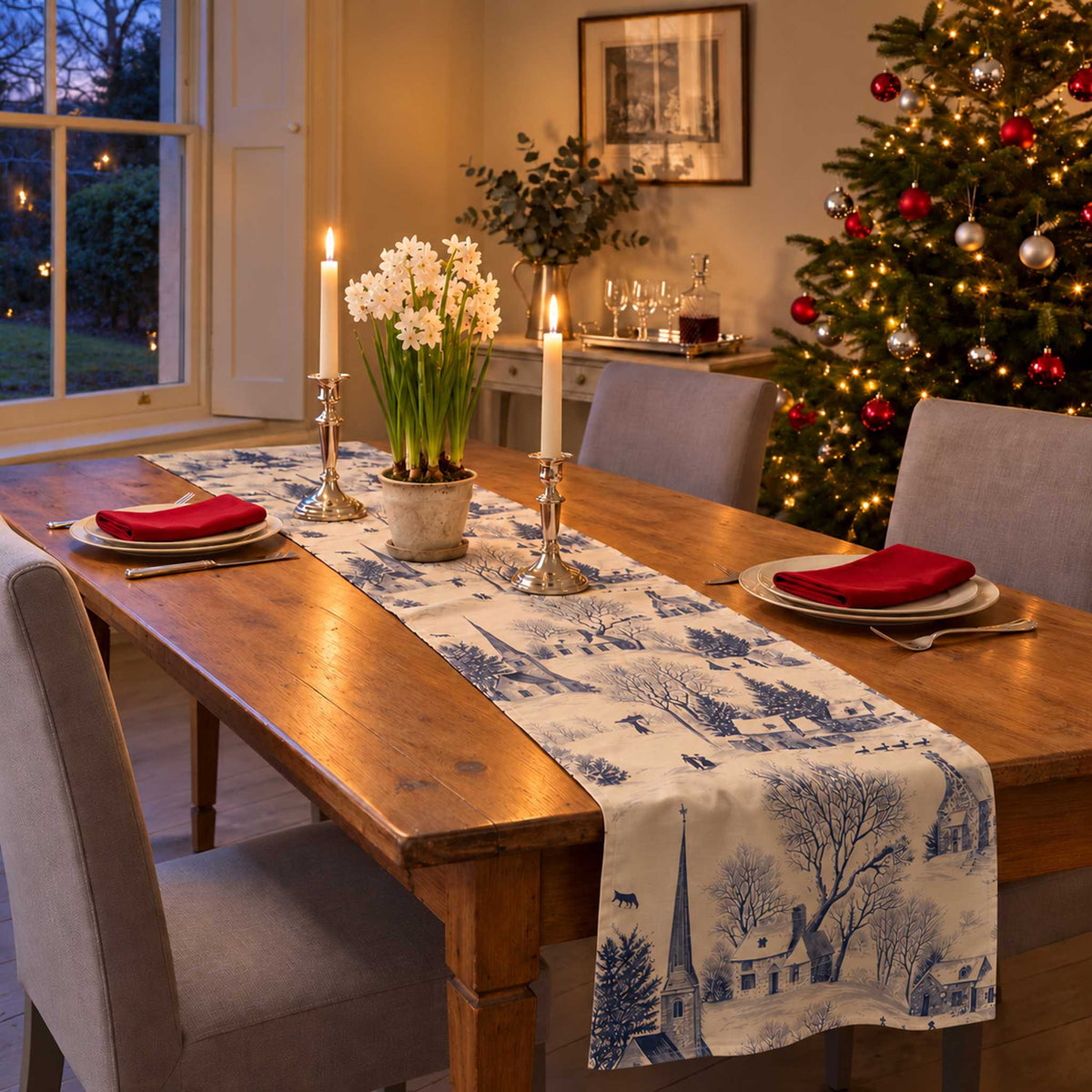 Village Toile Christmas table runner in Navy on ivory, styled on a wooden table with a softly draped end in a candlelit Christmas room.