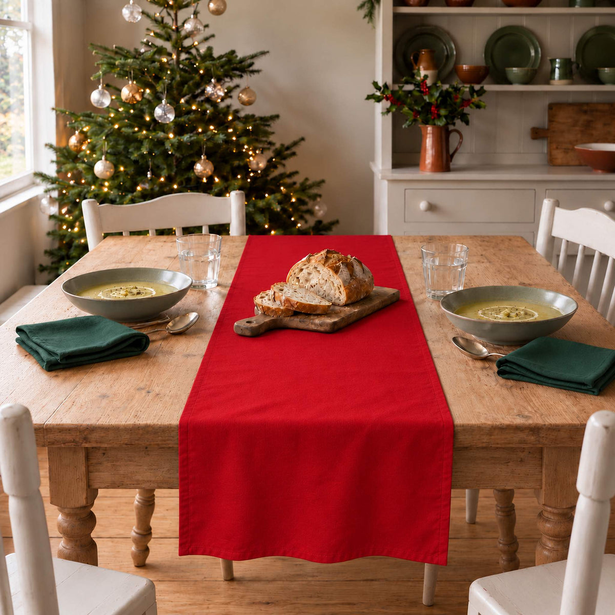 Plain Colours Christmas table runner in Red, styled on a wooden table with a softly draped end in a daylight Christmas room.