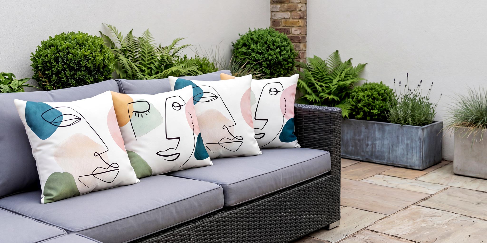 Abstract face-design outdoor garden cushions on a grey rattan sofa
