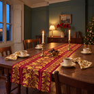 Gilded Ivy Christmas table runner in Burgundy and gold, styled on a wooden table with a softly draped end in a candlelit Christmas room.