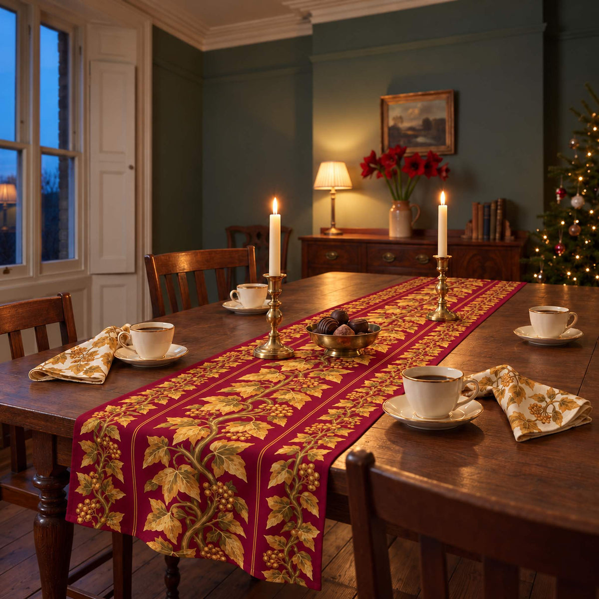 Gilded Ivy Christmas table runner in Burgundy and gold, styled on a wooden table with a softly draped end in a candlelit Christmas room.