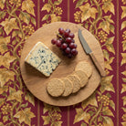 Burgundy and gold Gilded Ivy Christmas tablecloth with an oak cheeseboard, blue cheese, grapes and oatcakes