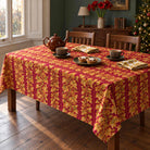 Burgundy and gold Gilded Ivy Christmas tablecloth on a rectangular wooden dining table, styled with a brown teapot, two cups and mince pies in a green room.