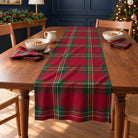 Tartan Christmas table runner in Burgundy, styled on a wooden table with a softly draped end in a daylight Christmas room.