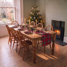 Burgundy tartan Christmas table runner with matching napkins on a wooden dining table beside a Christmas tree