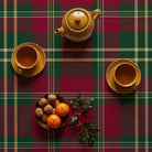 Burgundy tartan Christmas tablecloth seen from above, set for afternoon tea with a mustard teapot, two cups of tea, a bowl of walnuts and clementines and a sprig of holly