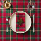 Burgundy tartan Christmas tablecloth seen from directly above, with a cream plate, a folded tartan napkin, a sprig of pine and a glass of red wine