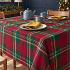 Burgundy Tartan Christmas tablecloth draped over a dining table with a blue-grey teapot, two mugs and gold napkins in soft daylight.