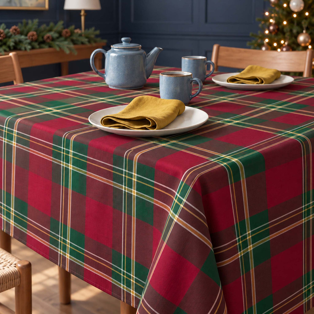 Burgundy Tartan Christmas tablecloth draped over a dining table with a blue-grey teapot, two mugs and gold napkins in soft daylight.