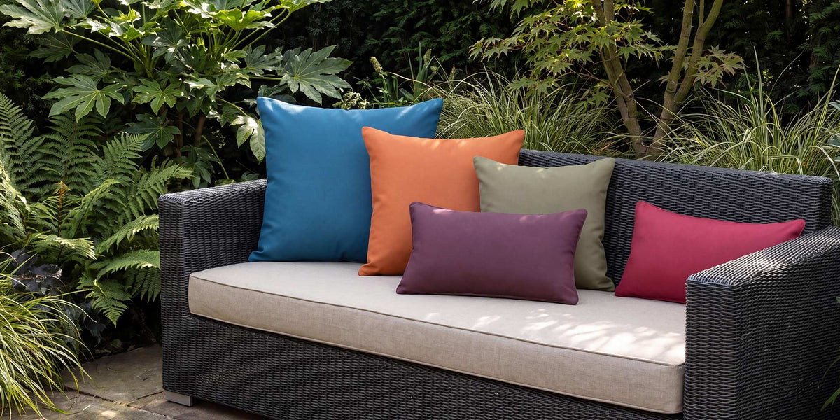 Colourful plain outdoor cushions in blue, orange, olive, grape and raspberry on a dark rattan garden sofa