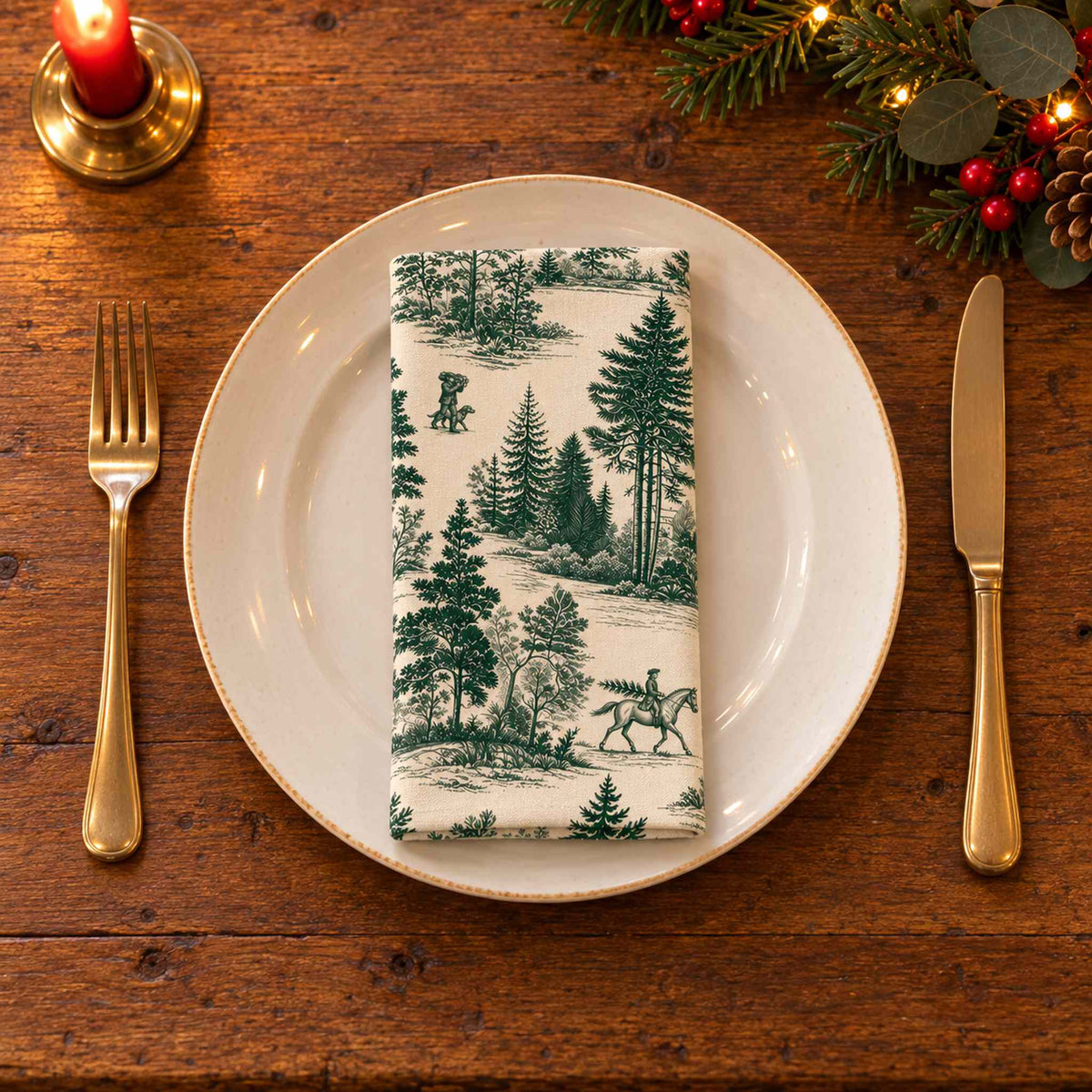 Green on ivory Fir Forest Toile cotton napkin neatly folded on a dinner plate with cutlery and candlelight on a wooden Christmas table.