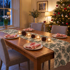 Pine Bough Christmas table runner in Green on ivory, styled on a wooden table with a softly draped end in a candlelit Christmas room.