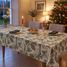 Green on ivory Pine Bough Christmas tablecloth draped over a dining table with green napkins, ivory plates, pears and candles in a pale Georgian room.