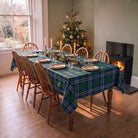 Green tartan Christmas tablecloth on a dining table laid for Christmas, beside a decorated tree and a lit wood burner