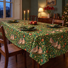 Green Turtle Doves and Mistletoe Christmas tablecloth draped over a dining table with green plates, folded napkins and candles in a green Victorian dining room.