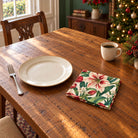 Ivory Amaryllis cotton napkin in a compact square fold beside a dinner plate and coffee cup on a wooden table in daylight.