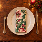 Ivory Amaryllis cotton napkin neatly folded on a dinner plate with cutlery and candlelight on a wooden Christmas table.