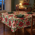 Ivory Amaryllis Christmas tablecloth draped over a dining table with green place settings and red candles in a green Victorian dining room.