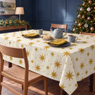 Ivory and gold Stars Christmas tablecloth draped over a dining table with a blue-grey tea set, shortbread and gold napkins in daylight.