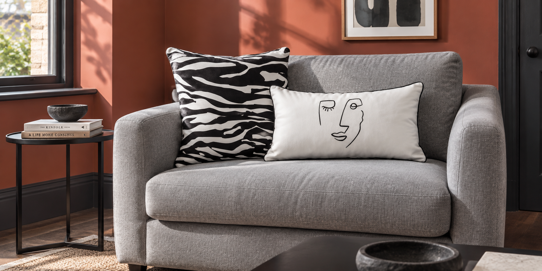 Black and white Zebra Print and Open Face velvet cushions on a light grey sofa against red walls.