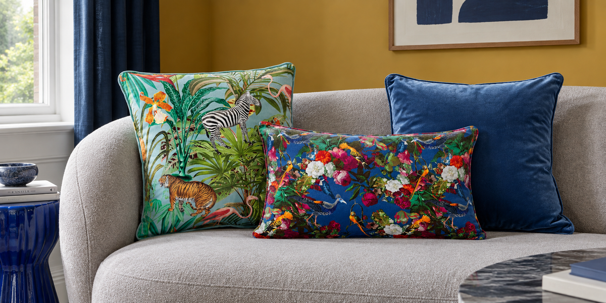 Blue Surf Jungle Fusion, Estate Blue Manor House Garden and plain Petrol Blue velvet cushions on a grey sofa.