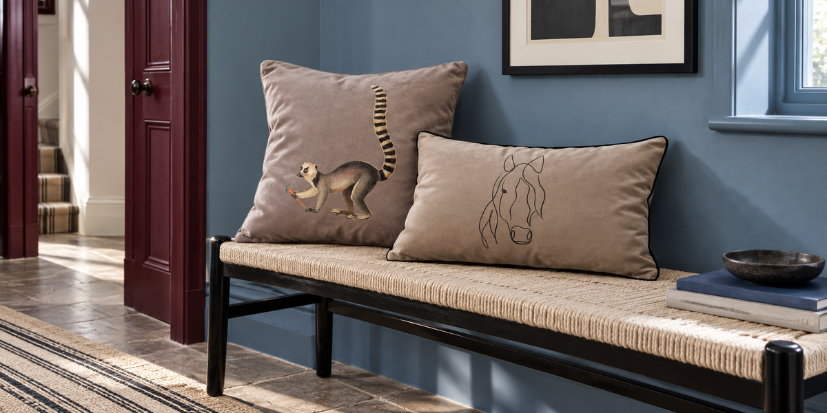 Dovedale Stone Lemur and Taupe Horse velvet cushions on a black bench in a blue painted hallway.