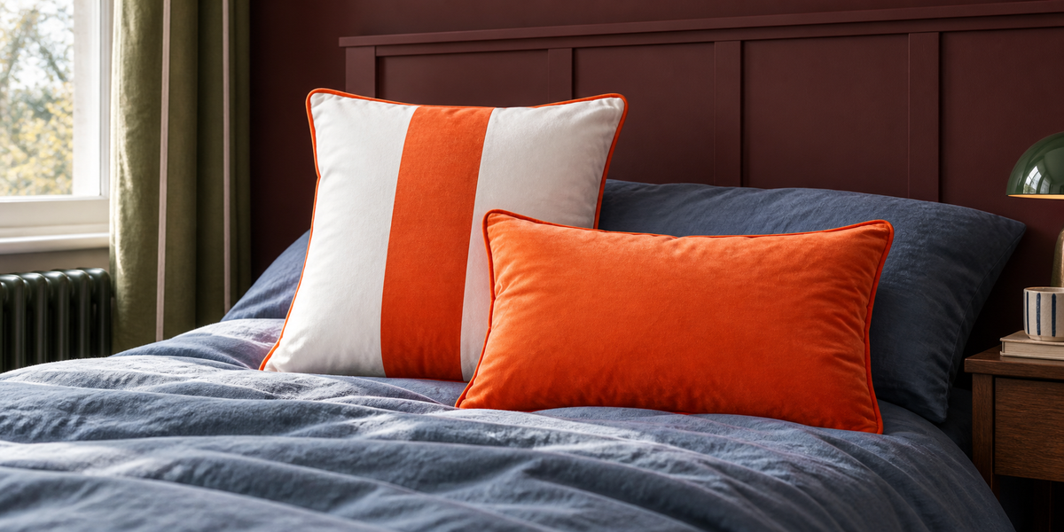 Burnt Orange striped square and plain rectangular velvet cushions on blue bedding with an oxblood headboard.
