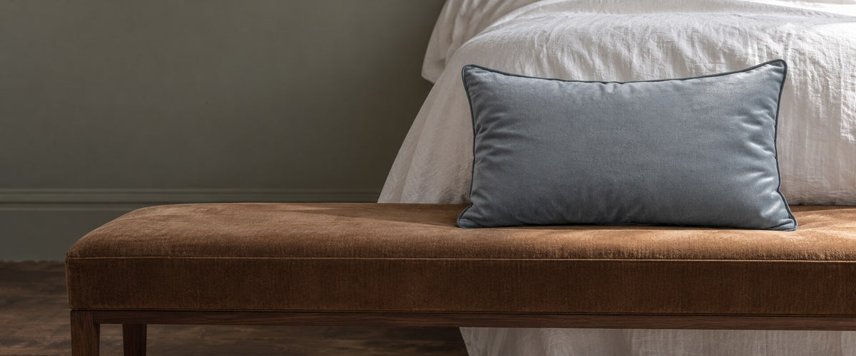 French Grey piped rectangular velvet cushion on a brown bench.