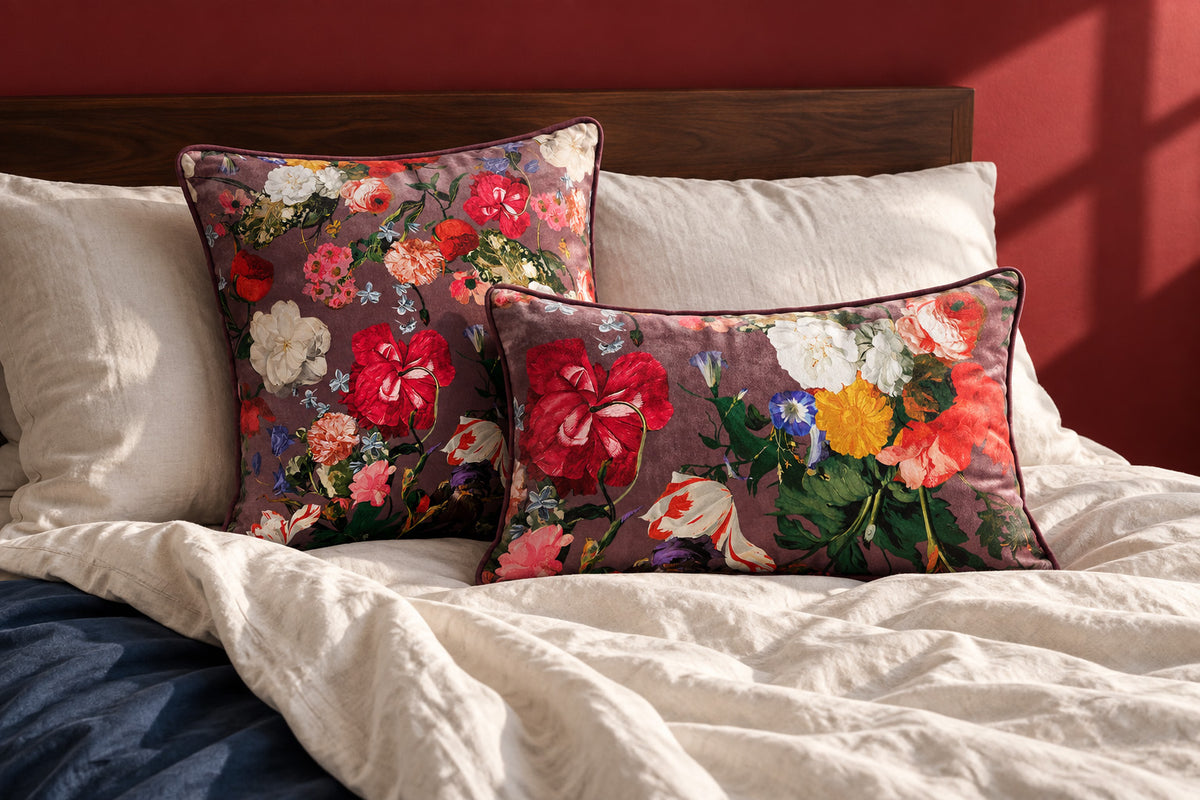 Garden Bouquet square and rectangular velvet cushions on a rumpled ivory bed with a dark wood headboard and oxblood wall.