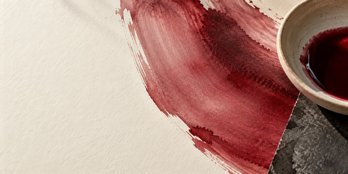 Garnet-red pigment, a ceramic dish and a curved brushstroke on ivory paper.