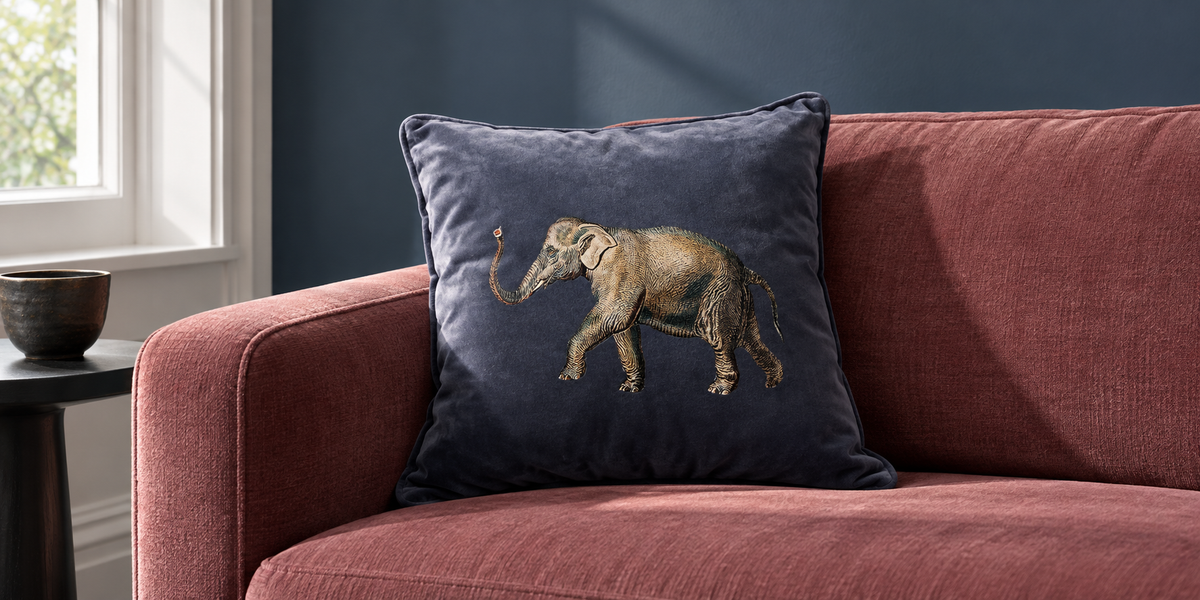 Graphite Elephant velvet cushion on a dusty rose sofa against a blue wall.