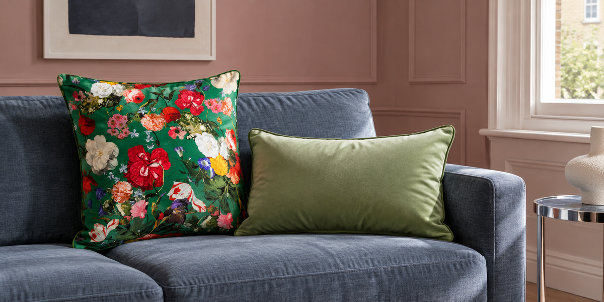 Emerald Green Garden Bouquet and plain Sage velvet cushions on a blue sofa against muted pink walls.