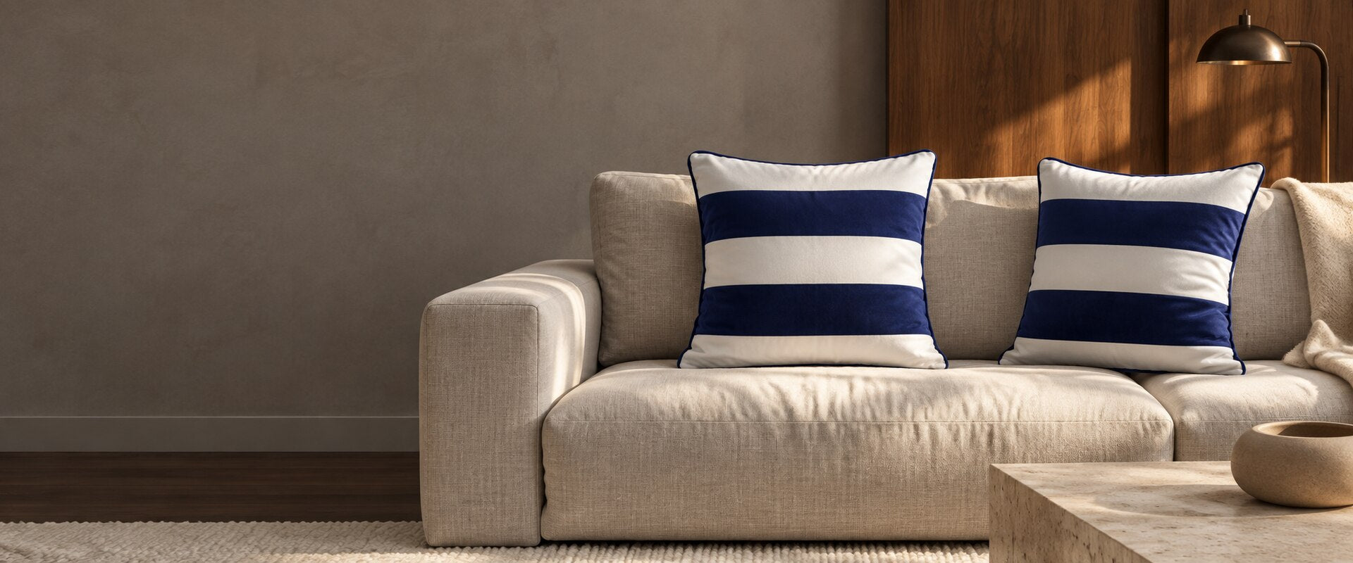 Midnight blue striped velvet cushions with piping on a pale sofa beside walnut panelling.