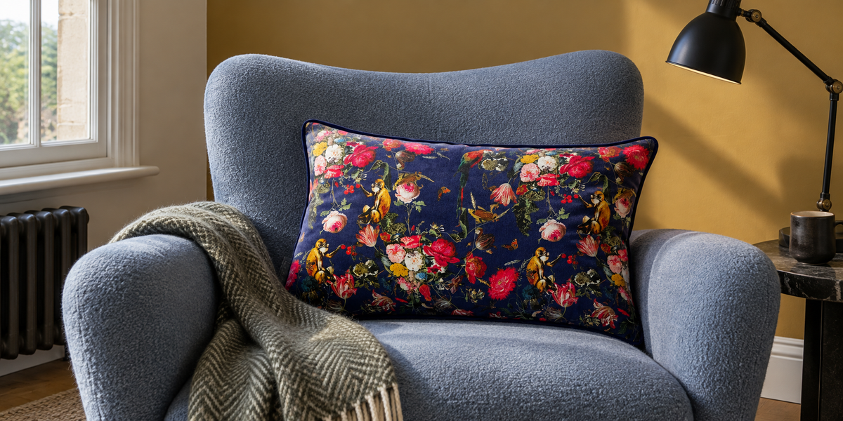 Midnight Monkey Puzzle rectangular velvet cushion in a mist blue reading chair against an ochre wall.