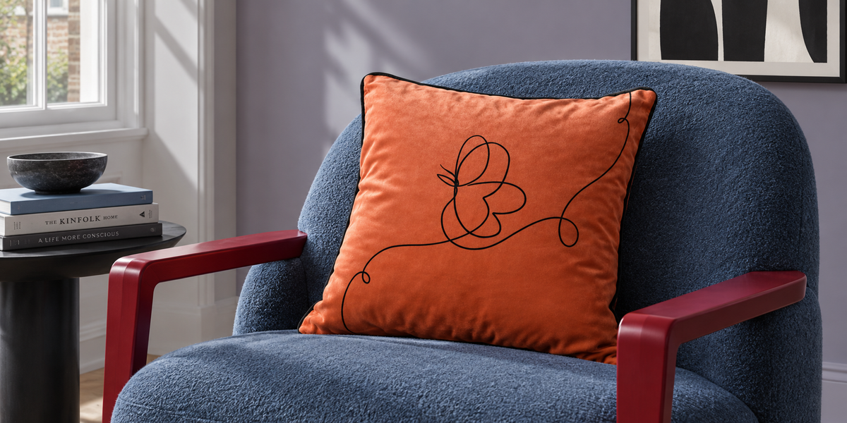 Burnt Ochre Butterfly velvet cushion on a blue chair with red wooden arms.