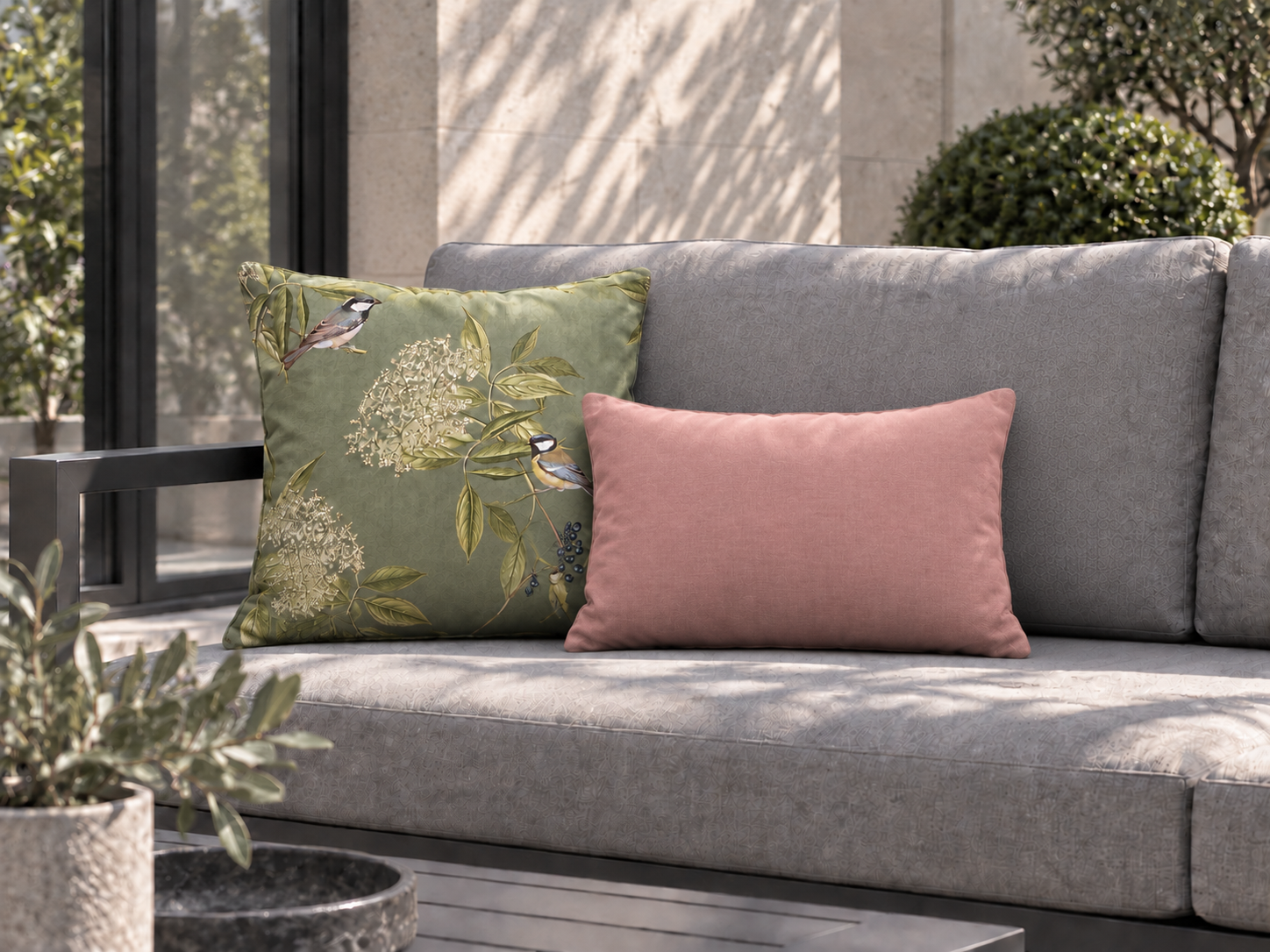 Standard sage bird-print square and compact blush rectangular cushions on a grey garden sofa.