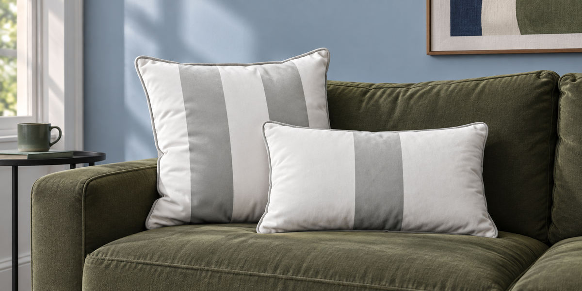 Storm Grey striped square and rectangular velvet cushions on an olive sofa against a powder blue wall.