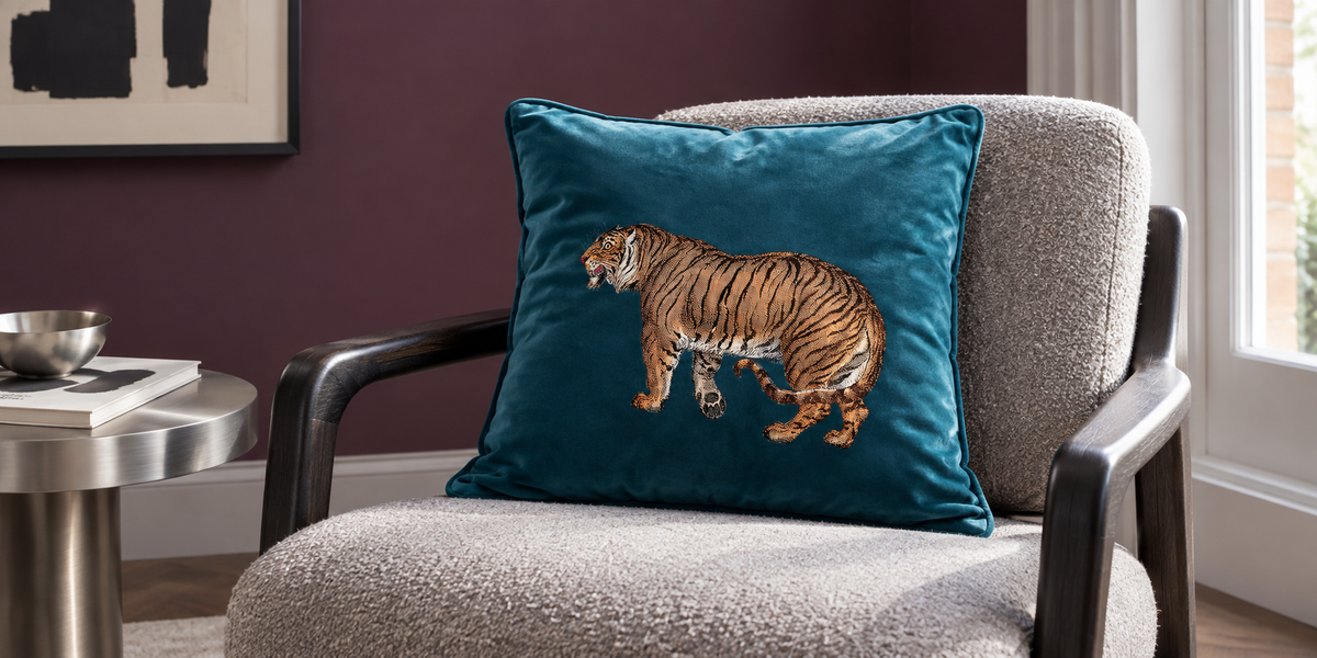 Petrol Blue Tiger velvet cushion on a pale grey reading chair against aubergine walls.