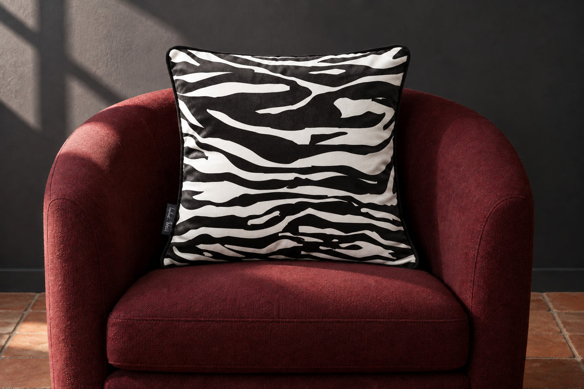 Black-and-white Zebra Print velvet cushion with black piping on a burgundy tub chair against a charcoal wall.